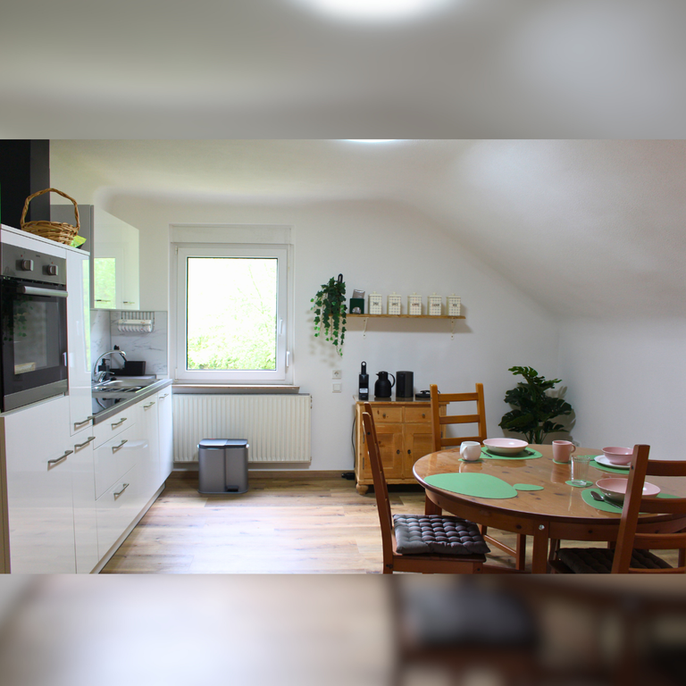 Wohnküche der Ferienwohnung Hahnekräh am Bostalsee mit hochwertiger Küchenzeile, Essbereich und Blick ins Grün.