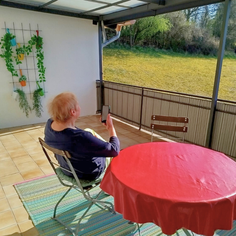 Frau sitzt am Balkontisch der Ferienwohnung Hanfdell mit Blick auf die grünen Wiesen – heller, einladender Balkon zum Entspannen