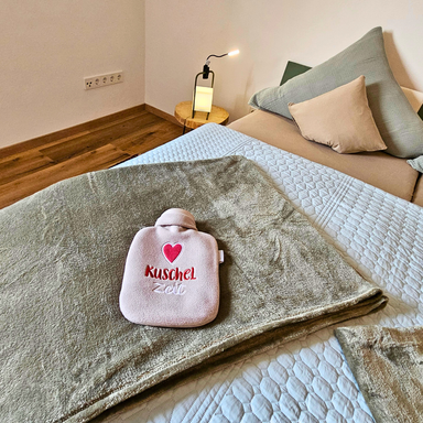 Schlafzimmerdetail der Ferienwohnung Hahnekräh mit winterlichen Bettaccessoires, Kuscheldecken, Bettfläschen und Leselampe.