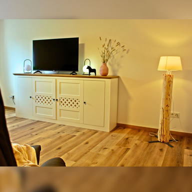 Wohnzimmer der Ferienwohnung Hahnekräh mit Highboard, Smart-TV und Stehlampe aus Holz aus eigenem Wald.